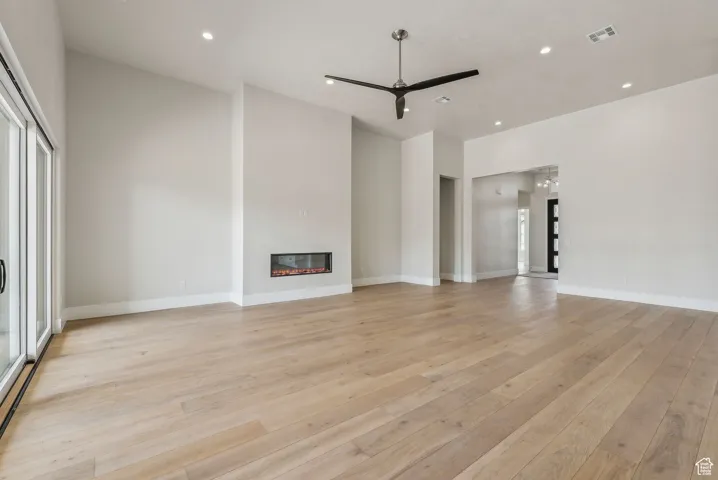 Unfurnished living room featuring visible vents, a glass covered fireplace, ceiling fan, recessed lighting, and light wood finished floors