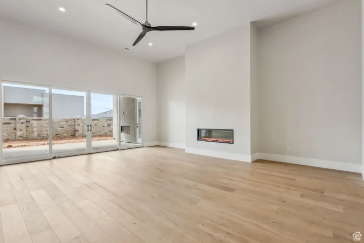 Unfurnished living room with a glass covered fireplace, baseboards, ceiling fan, light wood-type flooring, and recessed lighting