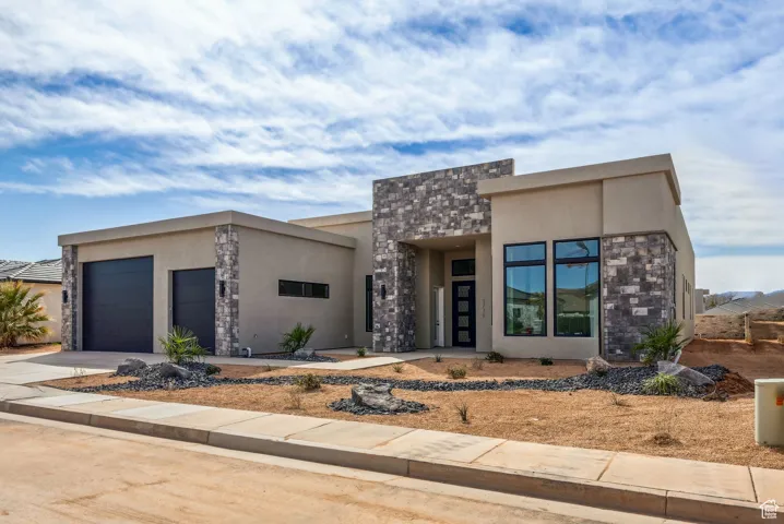 View of front of house featuring an attached garage, driveway, stone siding, and stucco siding