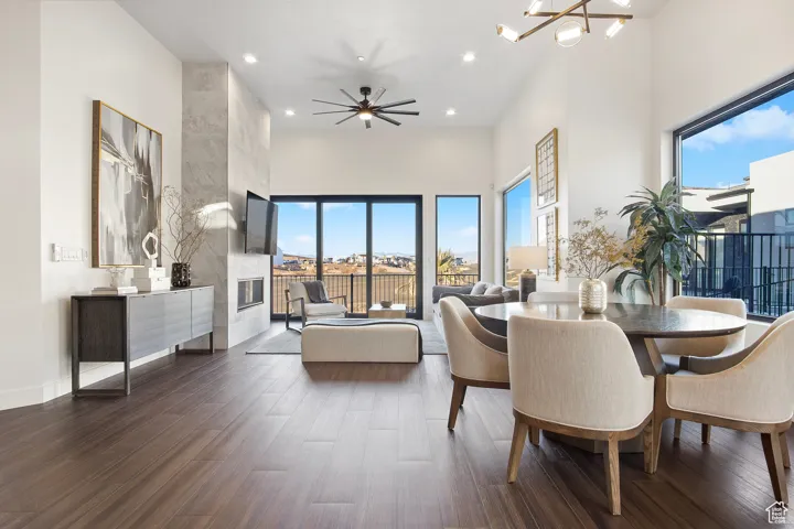 Dining area featuring ceiling fan with notable chandelier, a healthy amount of sunlight, a towering ceiling, and dark hardwood / wood-style floors