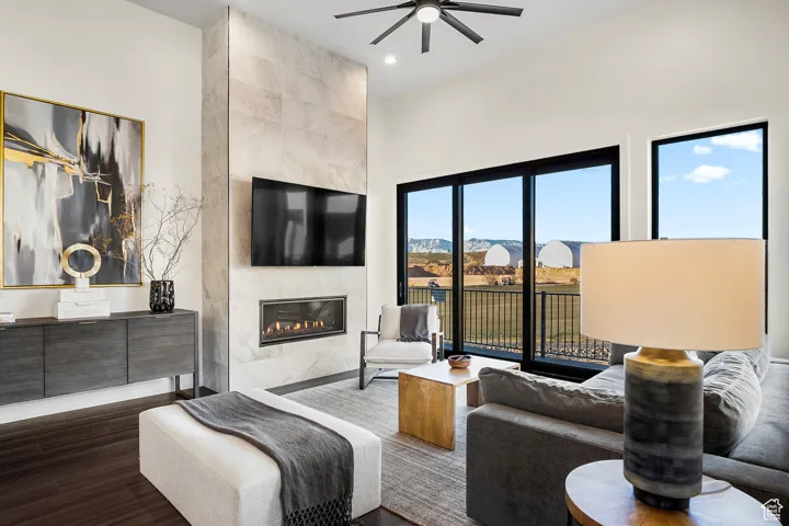 Living room featuring dark wood-type flooring, ceiling fan, and a fireplace
