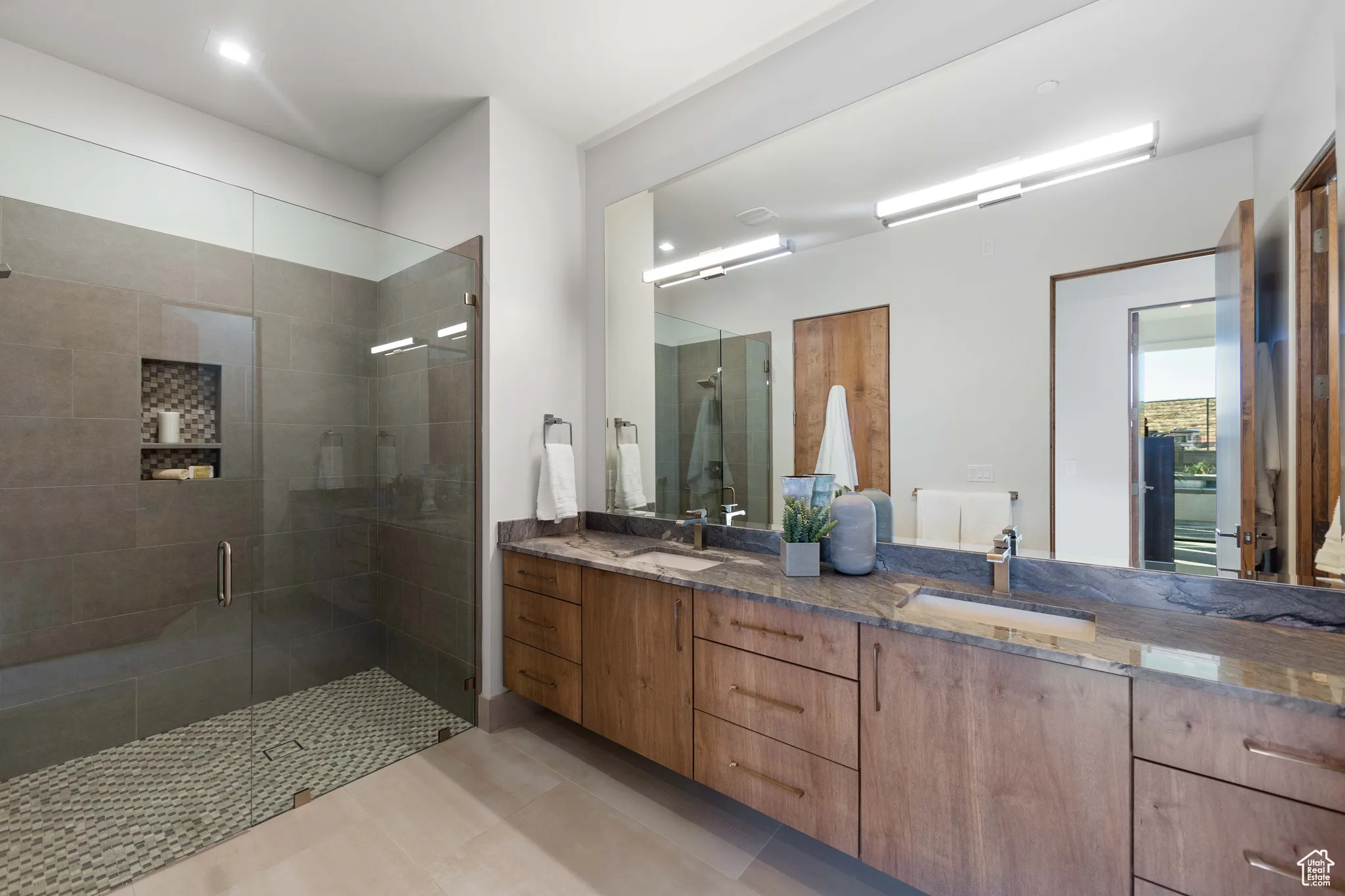 Bathroom featuring a shower with shower door, tile floors, and dual vanity