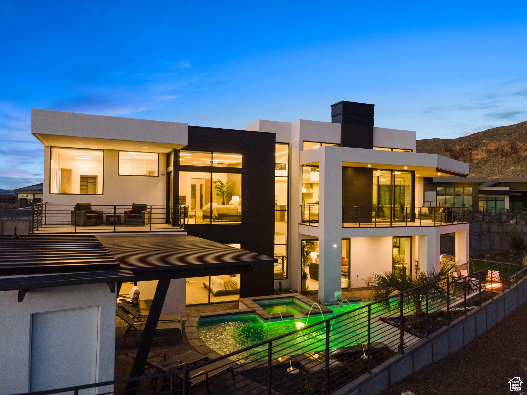 Back house at dusk featuring a balcony, a patio, and a pool with hot tub