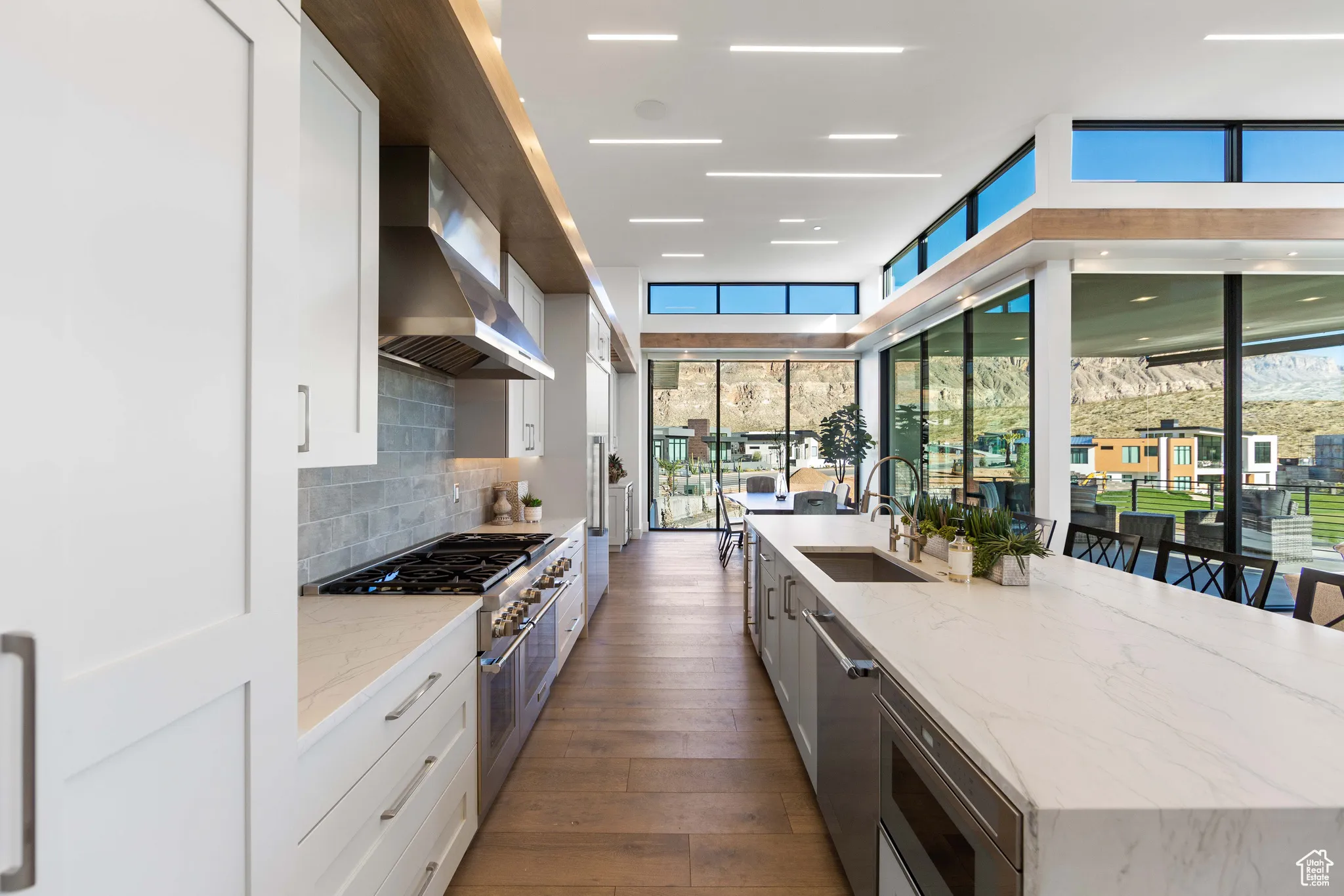 Kitchen with white cabinets, light stone countertops, dark hardwood / wood-style floors, wall chimney range hood, and stainless steel appliances