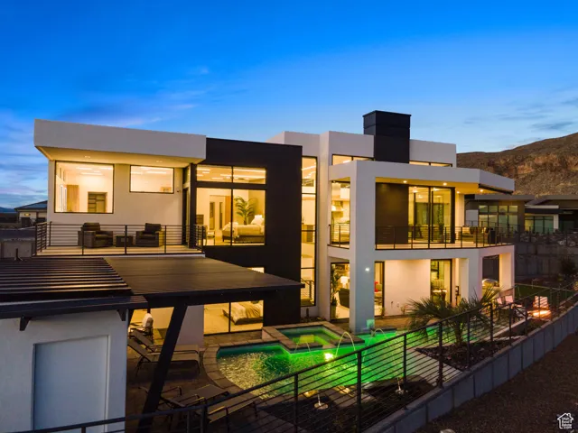 Back house at dusk featuring a balcony, a patio, and a pool with hot tub