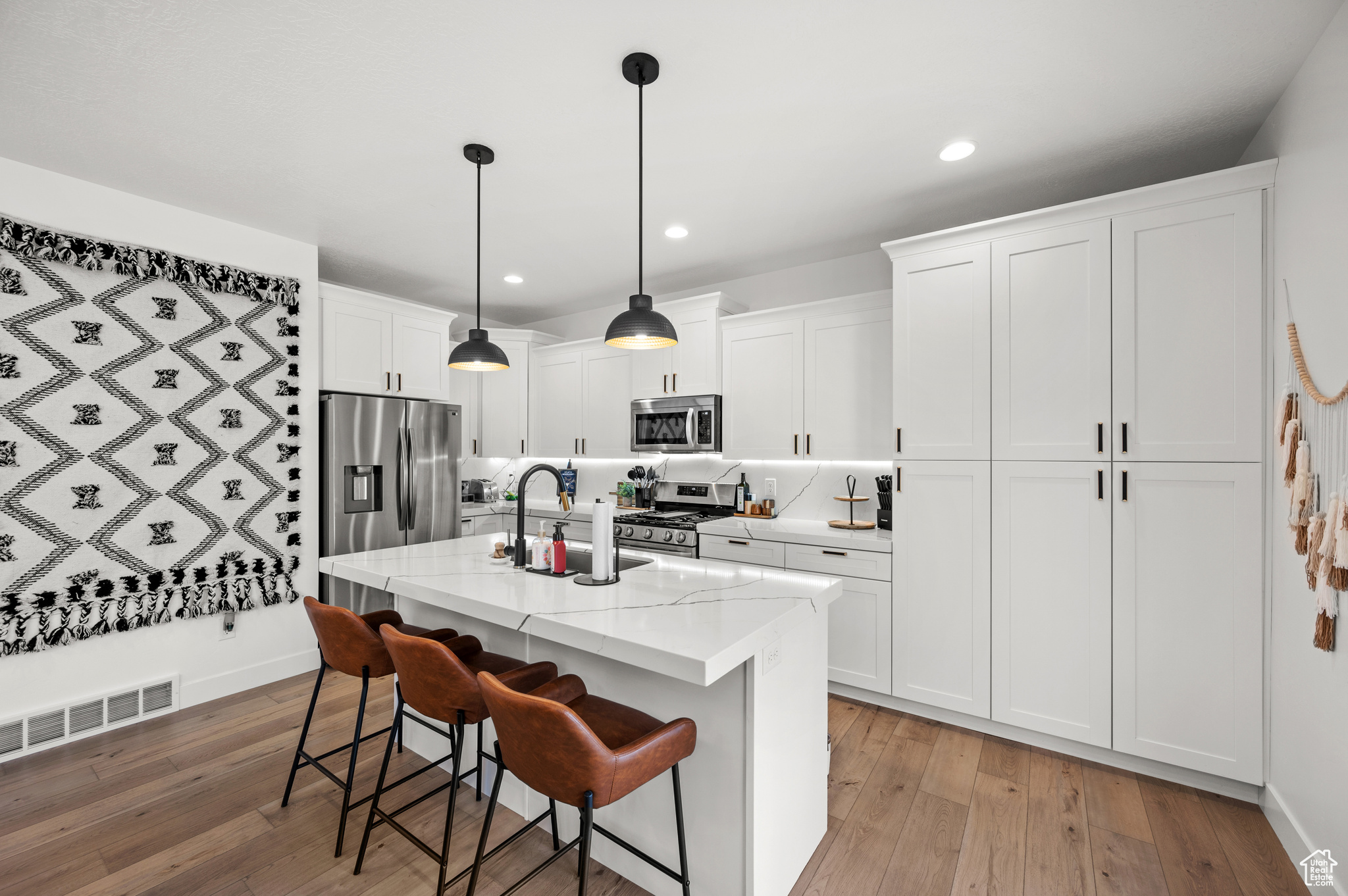 Kitchen featuring stainless steel appliances, white cabinets, a center island with sink, light hardwood / wood-style flooring, and decorative light fixtures