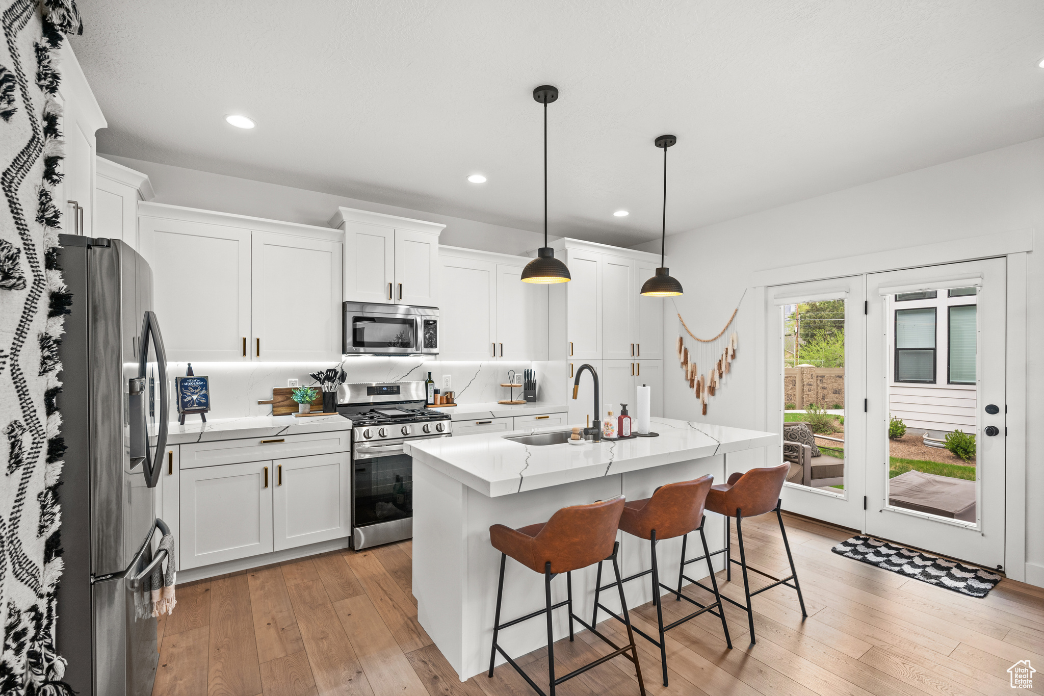 Kitchen with white cabinets, light hardwood / wood-style floors, appliances with stainless steel finishes, and an island with sink