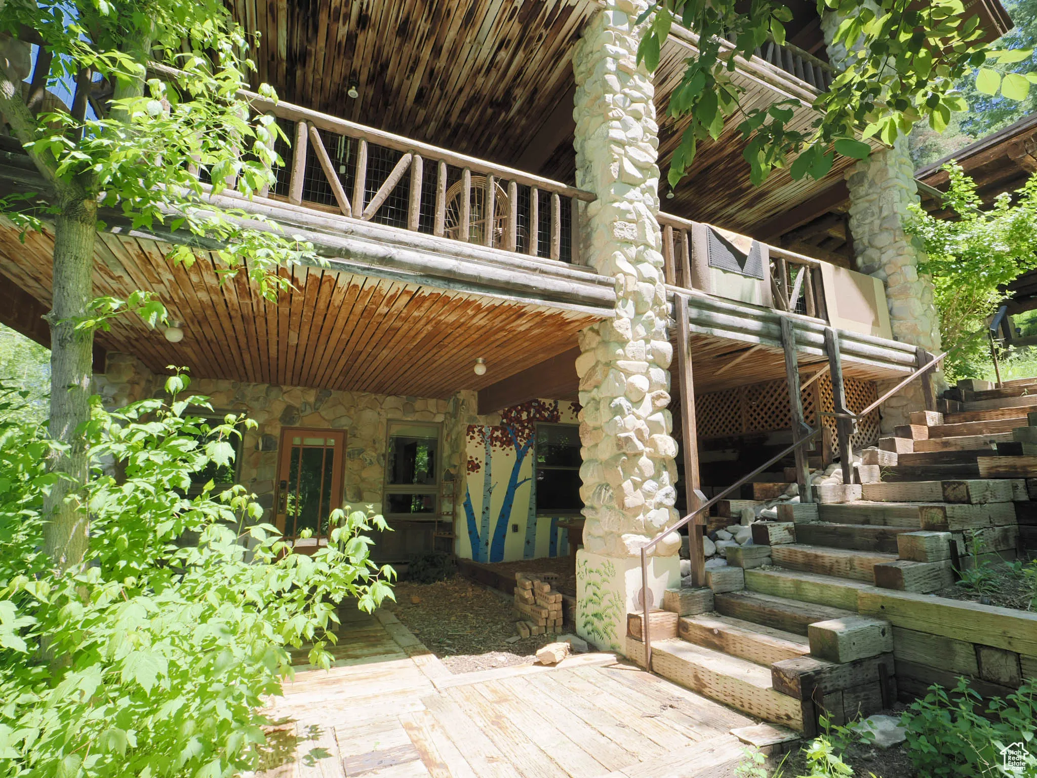 West side view of river stone columns and log handrails forming the porches