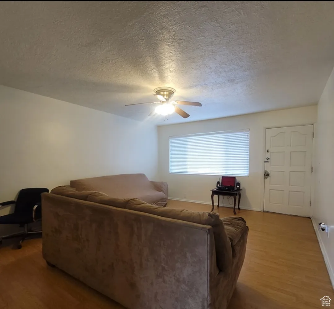 Living room with ceiling fan, a textured ceiling, and hardwood / wood-style flooring