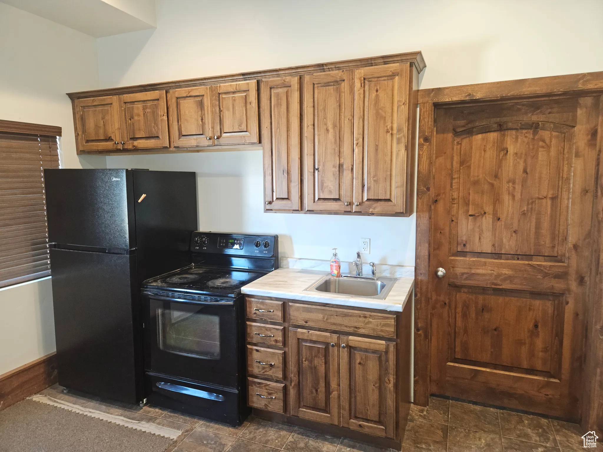 Kitchen with black appliances, a sink, light countertops, and brown cabinetry