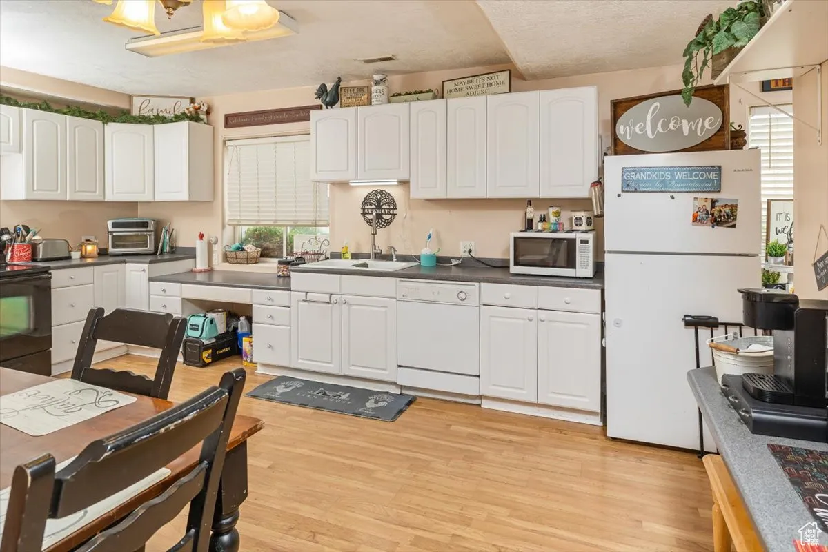 Kitchen (Basement) featuring sink, white cabinets, light wood-type flooring, and white appliances