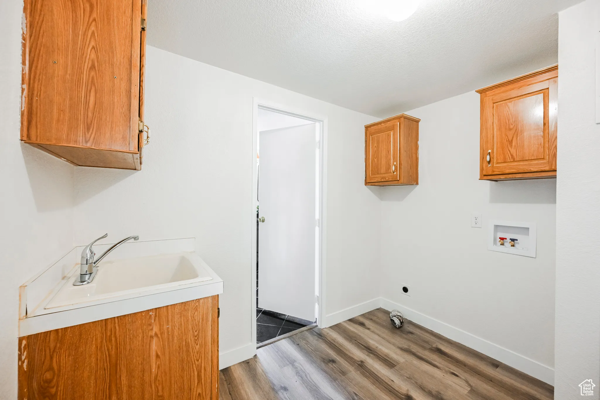 Clothes washing area with hardwood / wood-style floors, cabinets, a textured ceiling, sink, and washer hookup