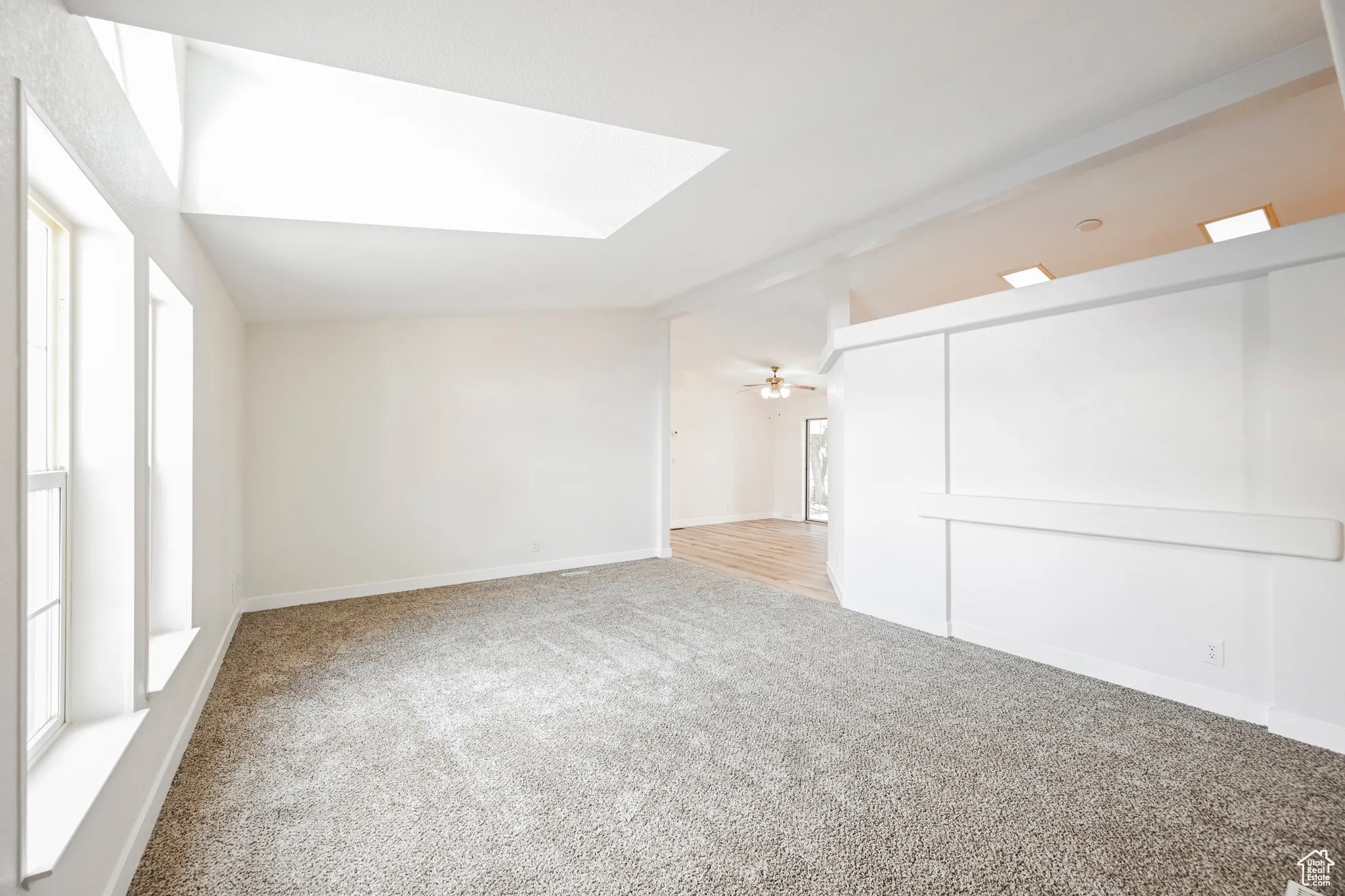 Carpeted spare room with ceiling fan, lofted ceiling with skylight, and a healthy amount of sunlight