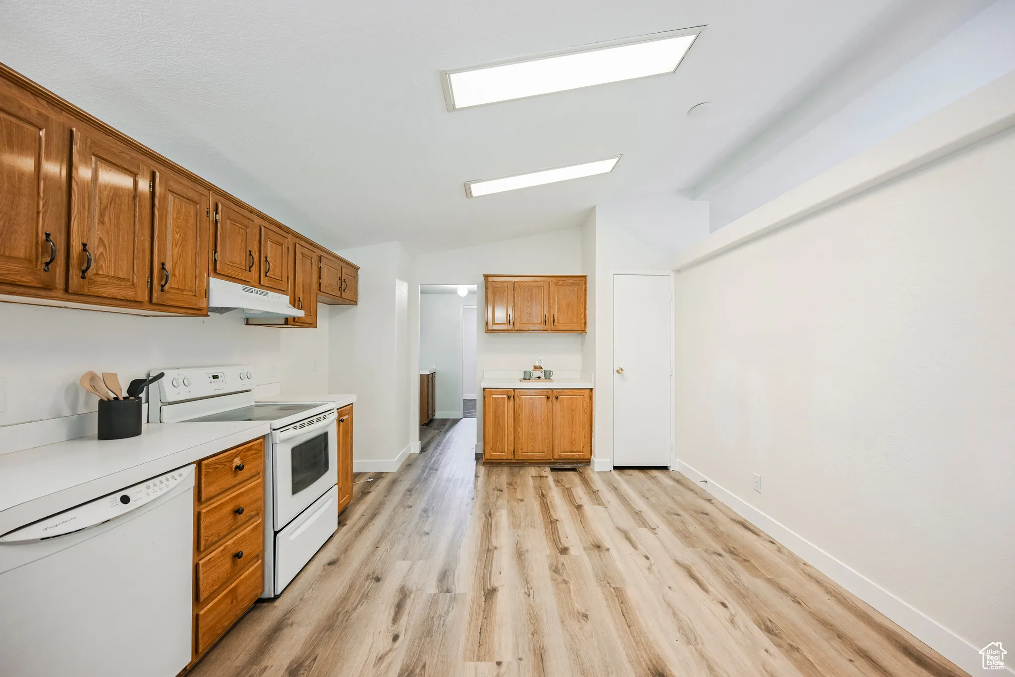 Kitchen with vaulted ceiling with skylight, white appliances, and light hardwood / wood-style floors