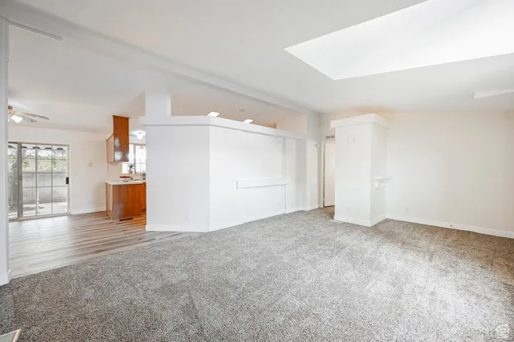Unfurnished living room featuring vaulted ceiling with skylight, light carpet, and ceiling fan
