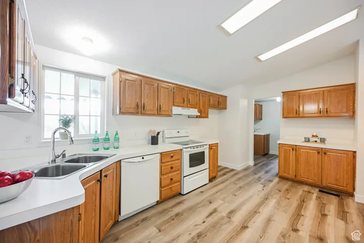 Kitchen with white appliances, light wood-type flooring, vaulted ceiling, and sink