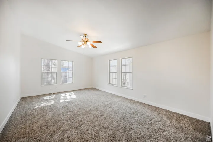 Empty room featuring ceiling fan, carpet, and lofted ceiling