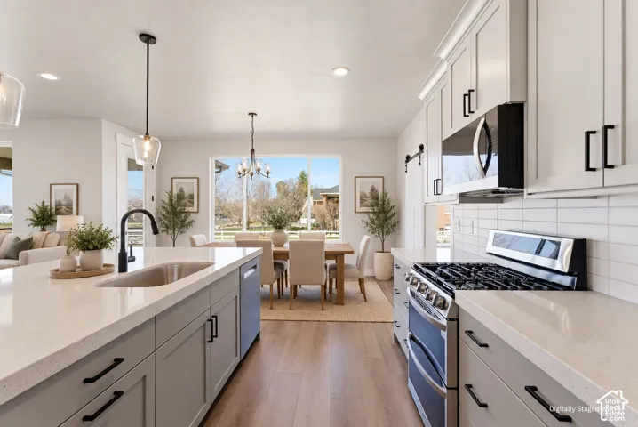 Spacious kitchen featuring an expansive island with an undermount sink, pendant lighting, and wood-finish flooring
