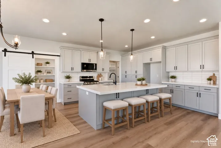 Open-concept kitchen and dining area featuring light-toned cabinetry, a large center island with seating, stainless steel appliances, and recessed lighting