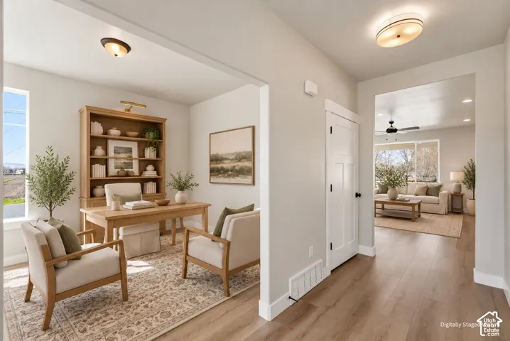 Light wood-finish flooring throughout, bright interior paint, and a wide entryway leading to a separate room with an exterior window