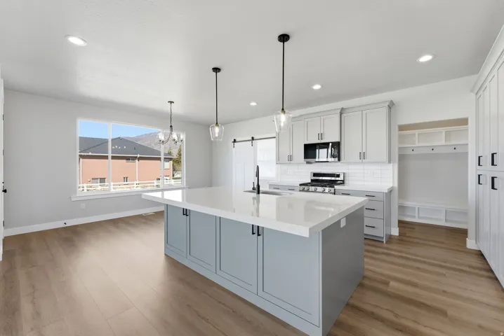 Kitchen with a barn door, stainless steel range with gas cooktop, light wood finished floors, a center island with sink, and tasteful backsplash