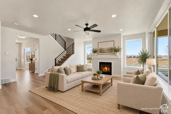 Recessed lighting, wood-finish flooring, a fireplace with a mantel, a black ceiling fan, and a staircase with black metal railings
