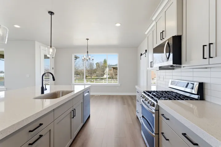 Kitchen featuring stainless steel appliances, light stone countertops, light wood-type flooring, tasteful backsplash, and suspended lighting