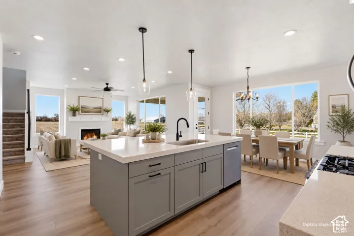 Open-concept living space featuring wood-finish flooring, a kitchen island with integrated sink, a built-in fireplace, and expansive windows