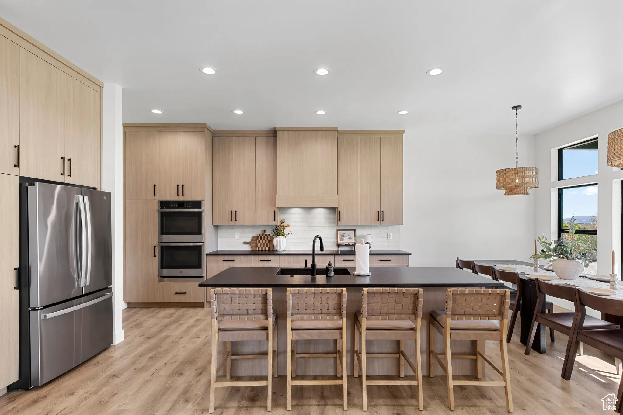 Kitchen with light brown cabinetry, appliances with stainless steel finishes, recessed lighting, light wood-style floors, and a kitchen island with sink