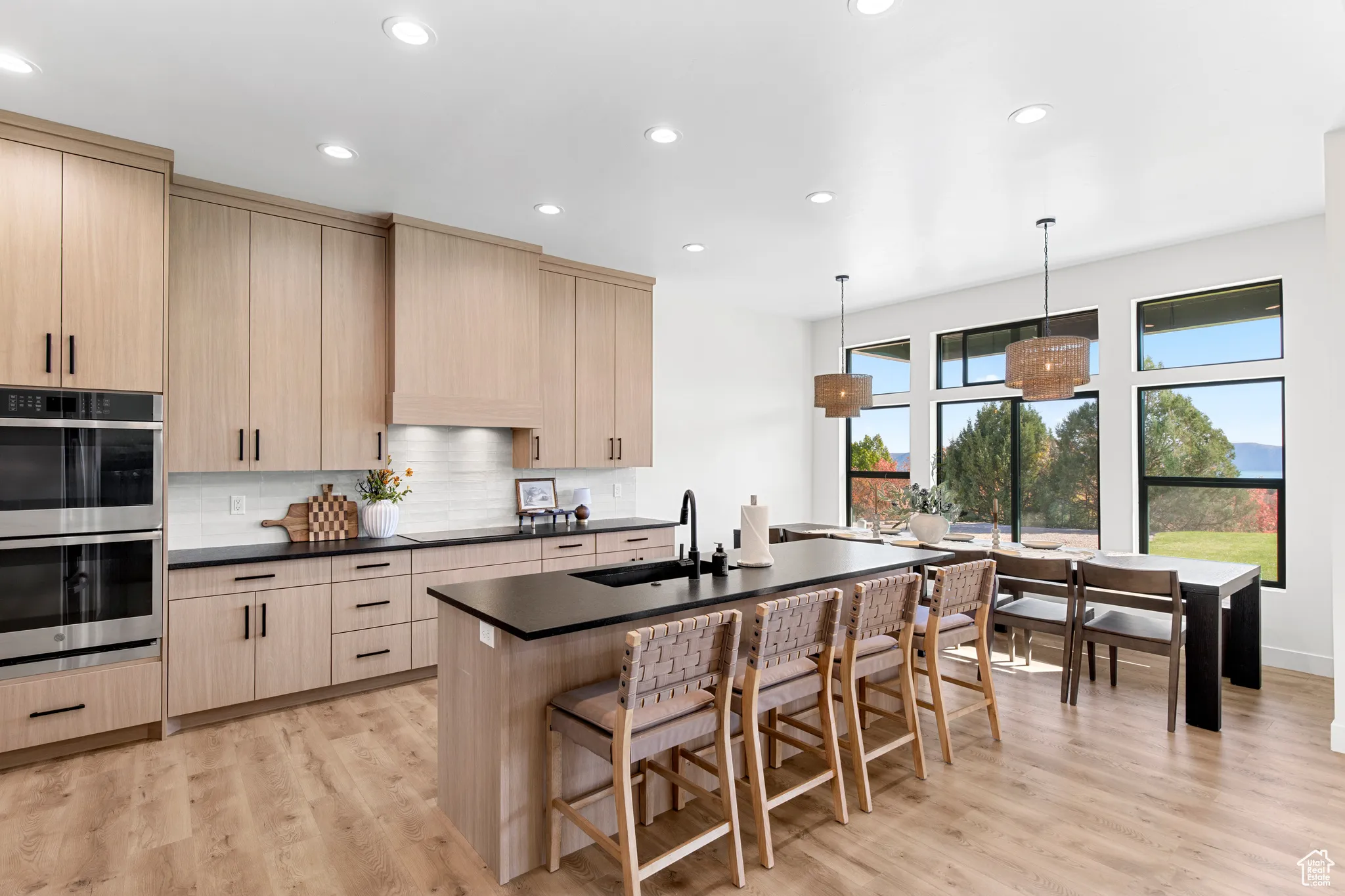 Kitchen featuring light brown cabinetry, stainless steel double oven, a kitchen island with sink, recessed lighting, and pendant lighting