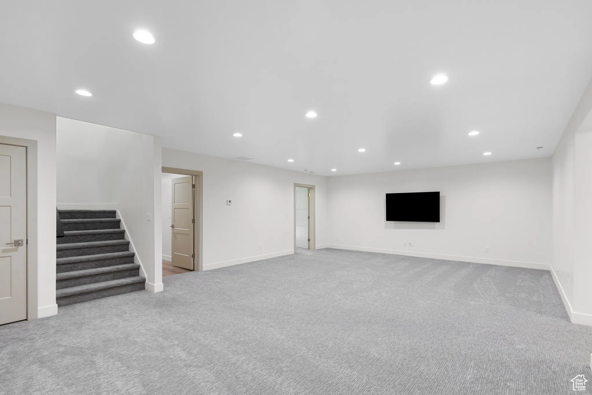 Unfurnished living room with recessed lighting, light colored carpet, and stairway