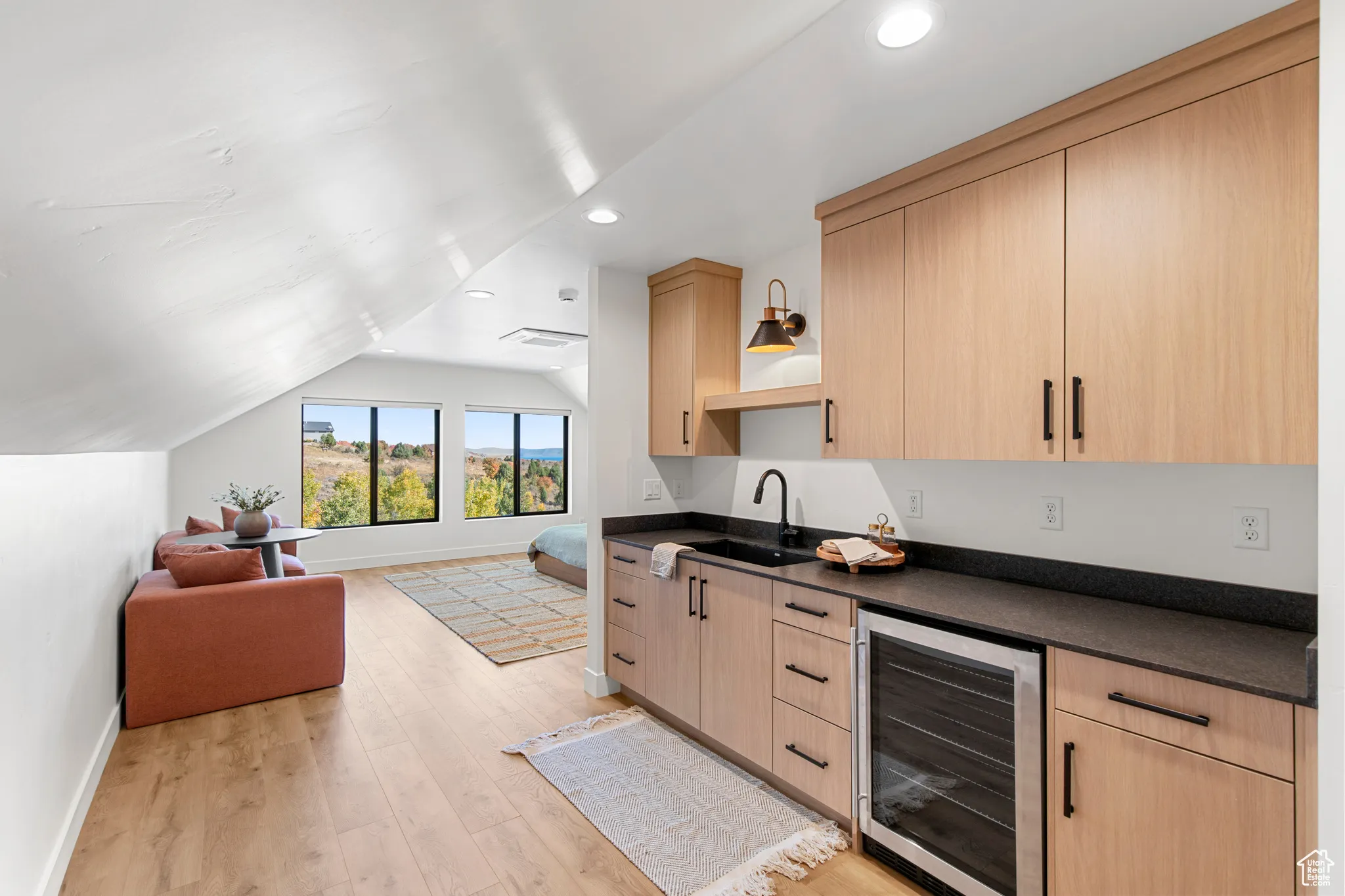 Bar area with light brown cabinetry, wine cooler, open shelves, light wood-style floors, and vaulted ceiling