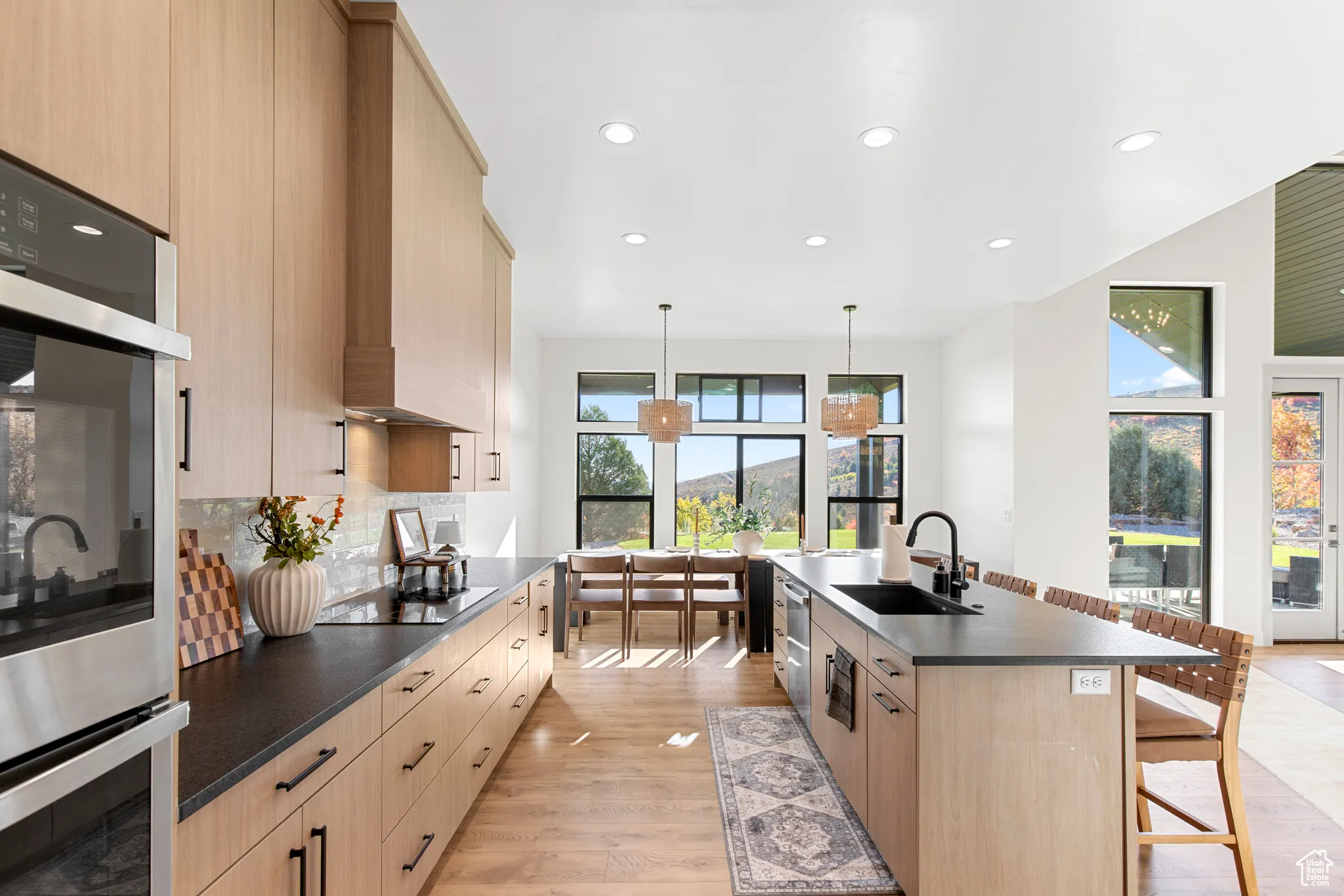 Kitchen featuring dark countertops, light brown cabinetry, stainless steel double oven, a kitchen breakfast bar, and recessed lighting