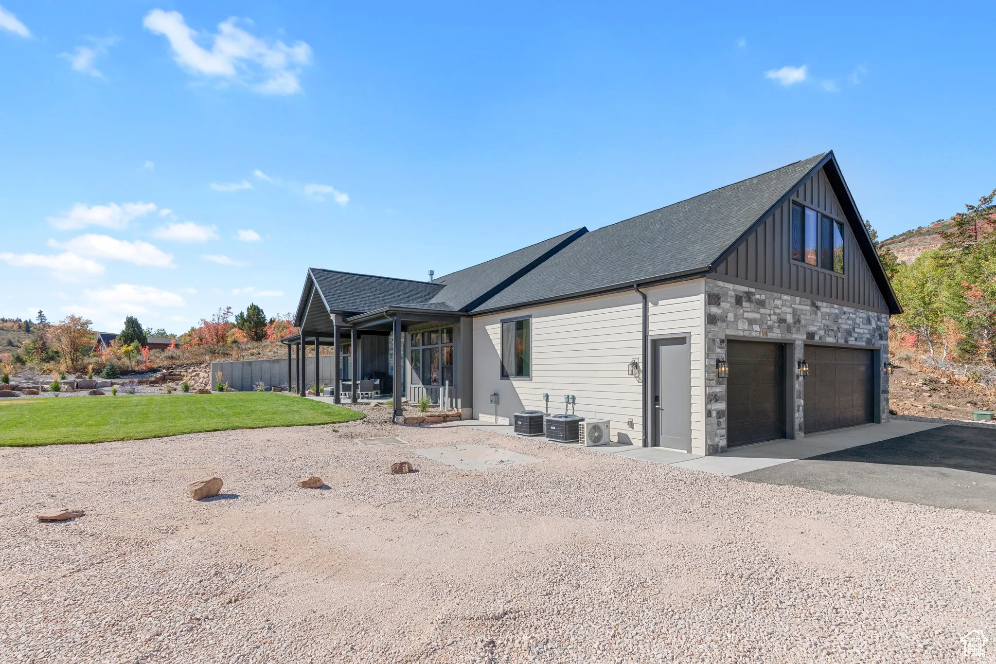 View of side of home featuring a garage, stone siding, a patio, driveway, and board and batten siding