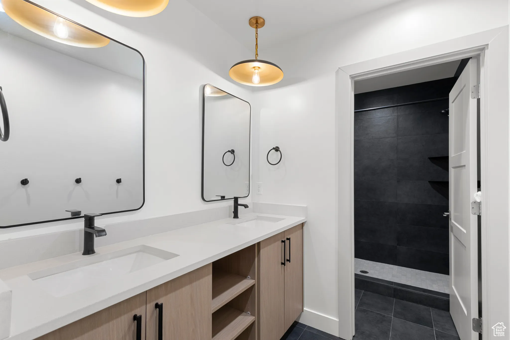 Bathroom featuring double vanity, a tile shower, and dark tile patterned flooring