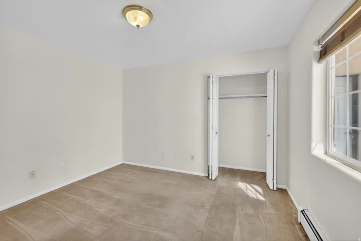 Unfurnished bedroom with a baseboard radiator, light carpet, and a closet