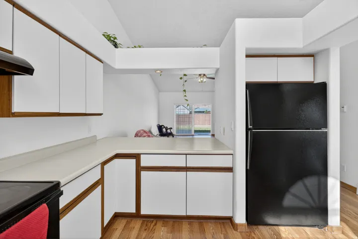 Two tone kitchen with two tone cabinets, black appliances, light countertops, light wood-type flooring, and a ceiling fan