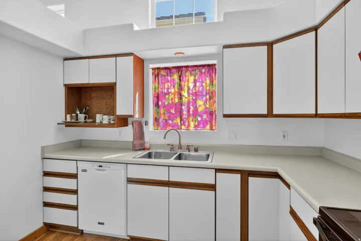 Kitchen featuring dual tone cabinetry, healthy amount of natural light, dishwasher, black range oven, and light countertops