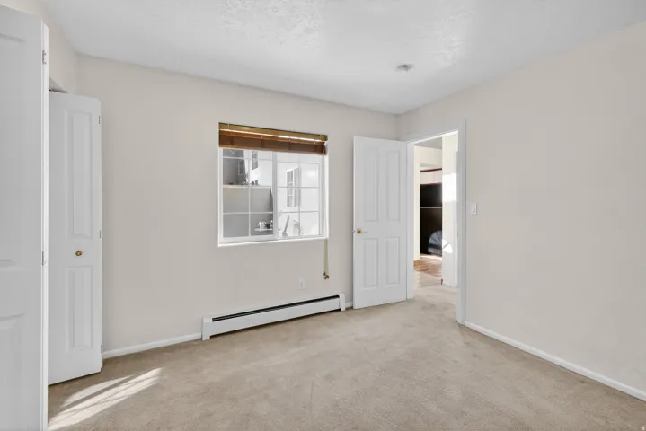 Unfurnished bedroom featuring a baseboard radiator and light carpet