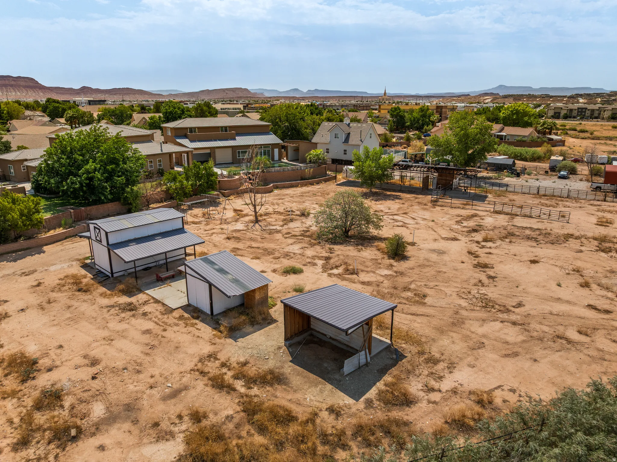 Barn, tack room, and shelters across open ground, red rock ridgeline in every direction.