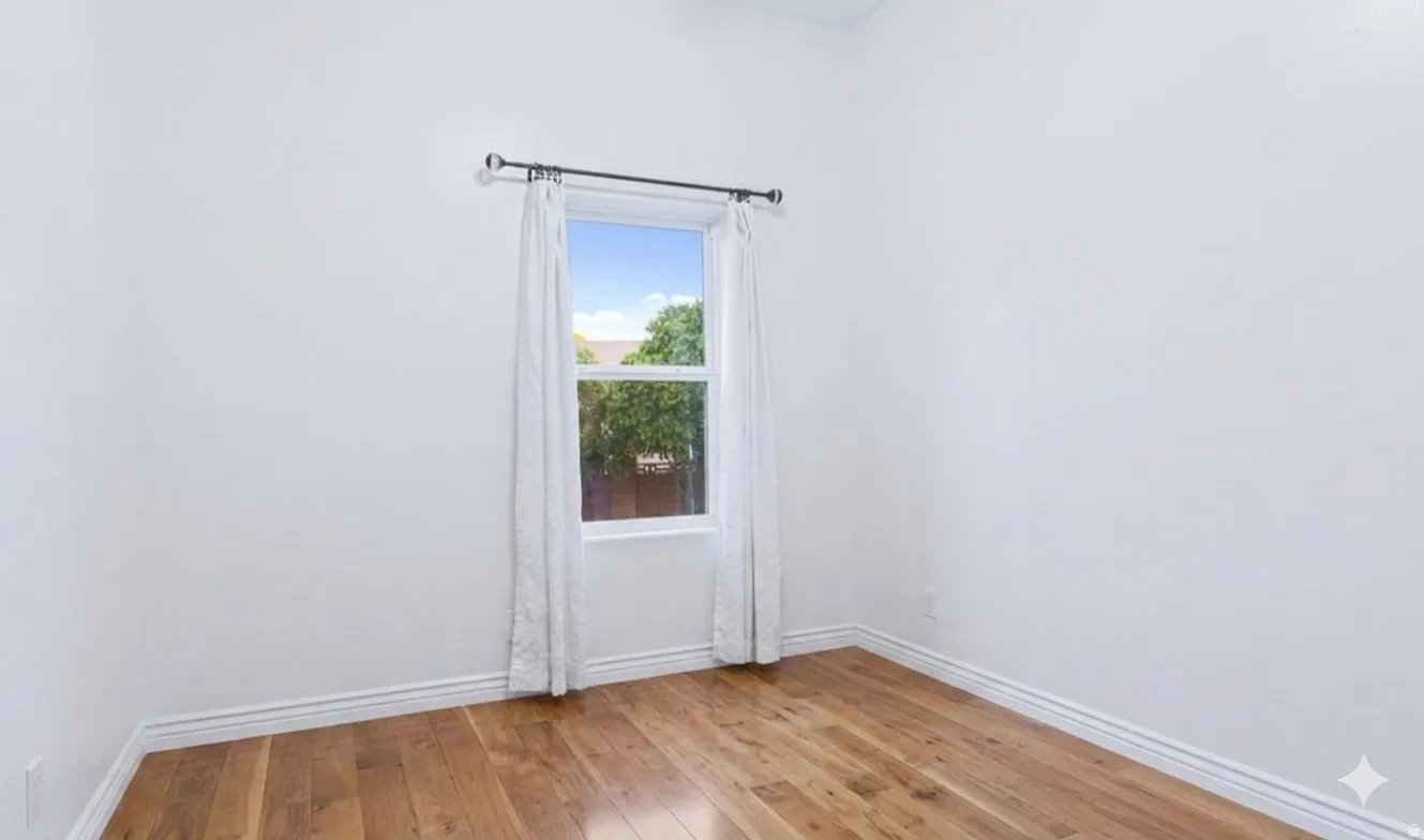 Main-level bedroom with hardwood and yard-facing window.