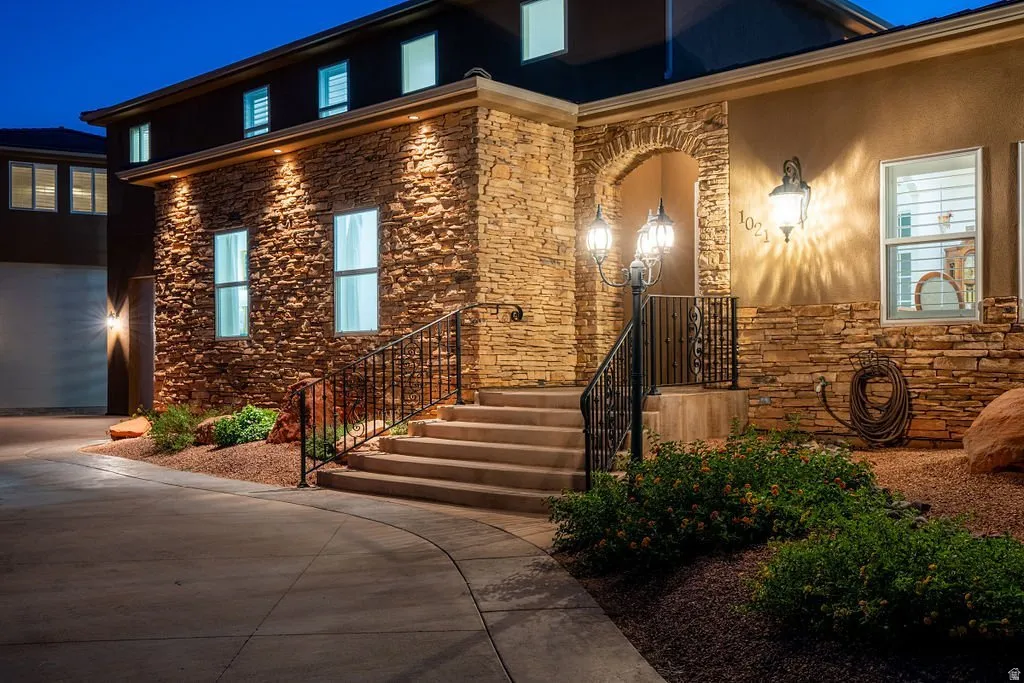Stacked stone, warm landscape lighting, and a wide stair rise to the front door.