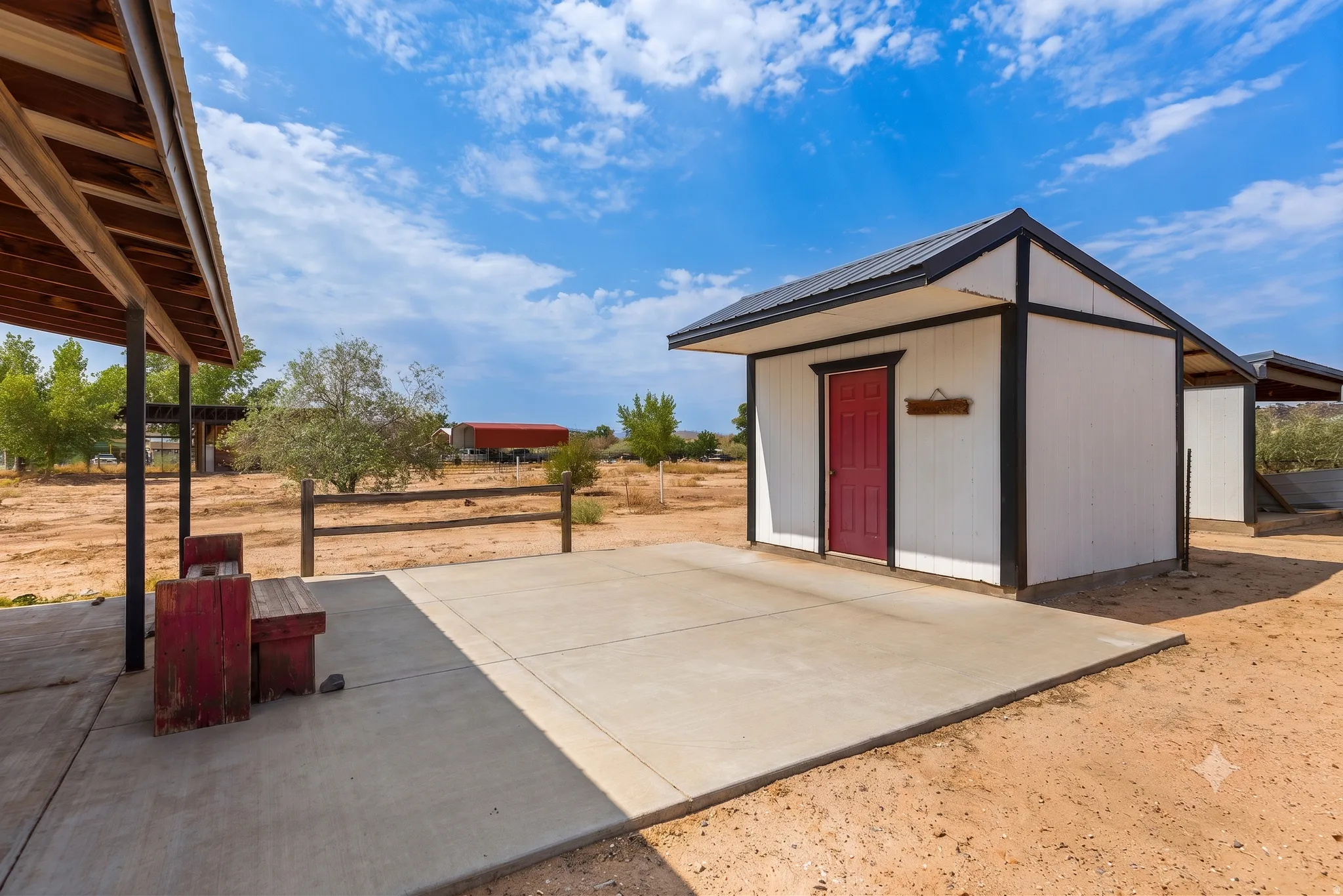 Purpose-built tack room with covered breezeway and a wide concrete apron connecting the outbuildings. No mud between you and your gear.