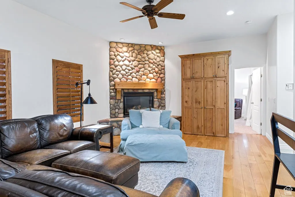 Living room with light hardwood / wood-style flooring, ceiling fan, and a stone fireplace