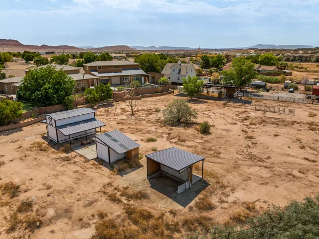 Barn, tack room, and shelters across open ground, red rock ridgeline in every direction.