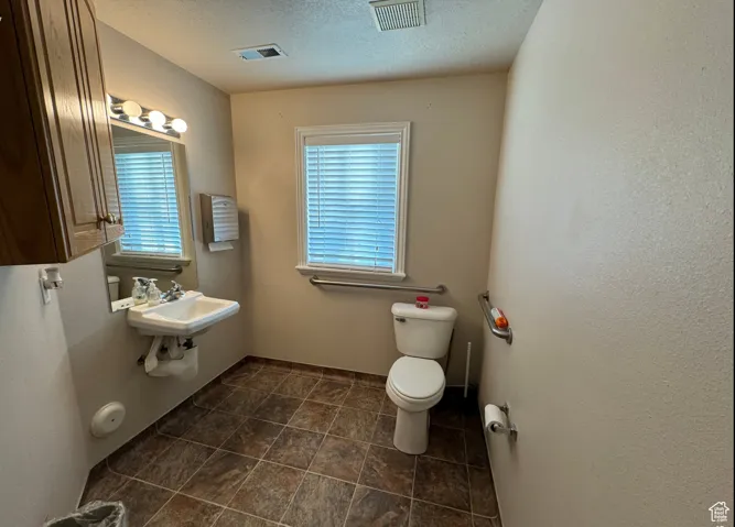 Bathroom featuring a textured ceiling, toilet, sink, and a wealth of natural light