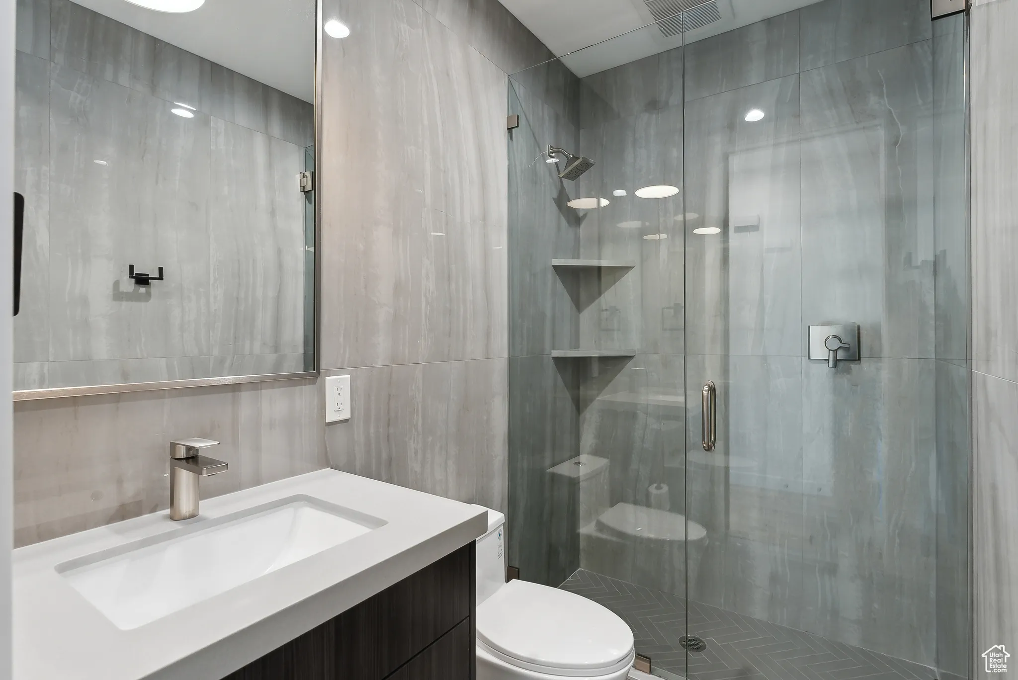 Bathroom with tile walls, vanity, toilet, and an enclosed shower