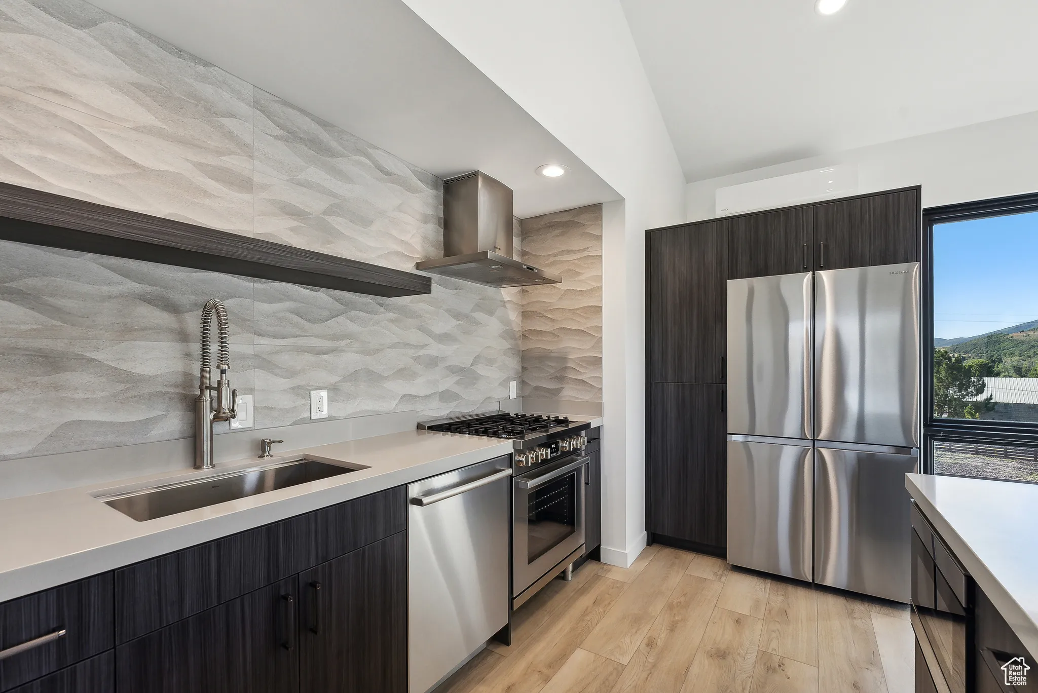 Kitchen with lofted ceiling, sink, wall chimney exhaust hood, light hardwood / wood-style flooring, and appliances with stainless steel finishes