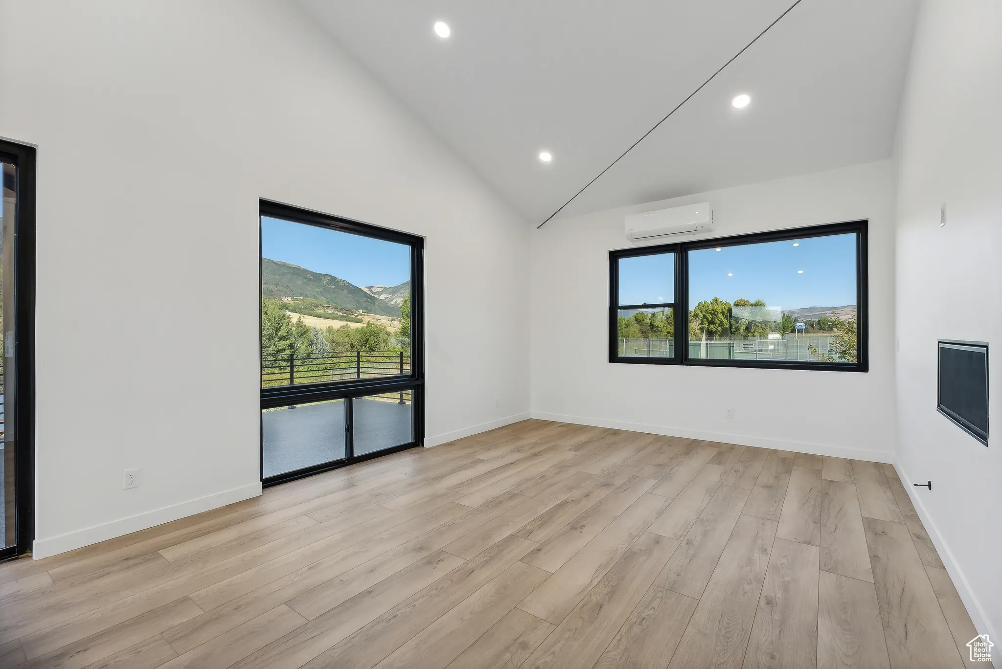 Empty room featuring high vaulted ceiling, light wood-type flooring, and a wall mounted AC