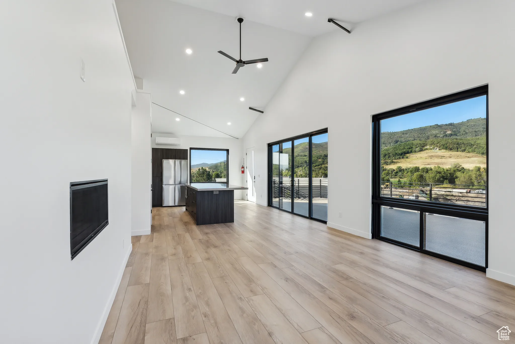 Unfurnished living room featuring high vaulted ceiling, an AC wall unit, light hardwood / wood-style floors, and ceiling fan